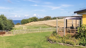 A vineyard with a wooden fence, a pergola with a table and chairs, and a view of the sea. - Awesome apartment in Hasle (Hasle)