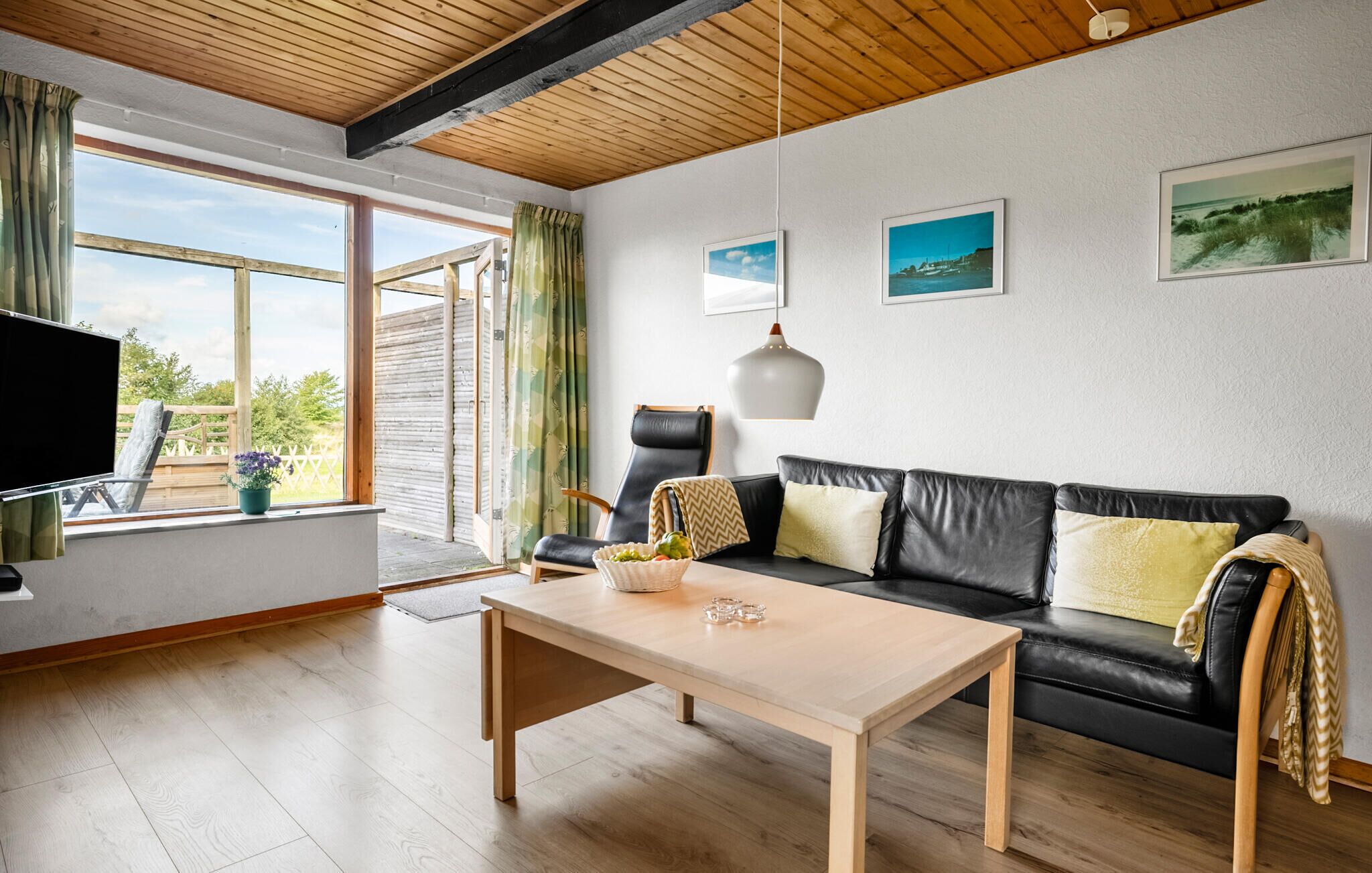 Una sala de estar moderna con techo de madera, un sofá de cuero negro, una mesa de centro de madera y un televisor sobre un mueble.