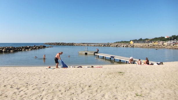 A beach with a wooden pier extending into calm waters, a sandy shore, and a rocky breakwater in the background. - Awesome apartment in Hasle (Hasle)