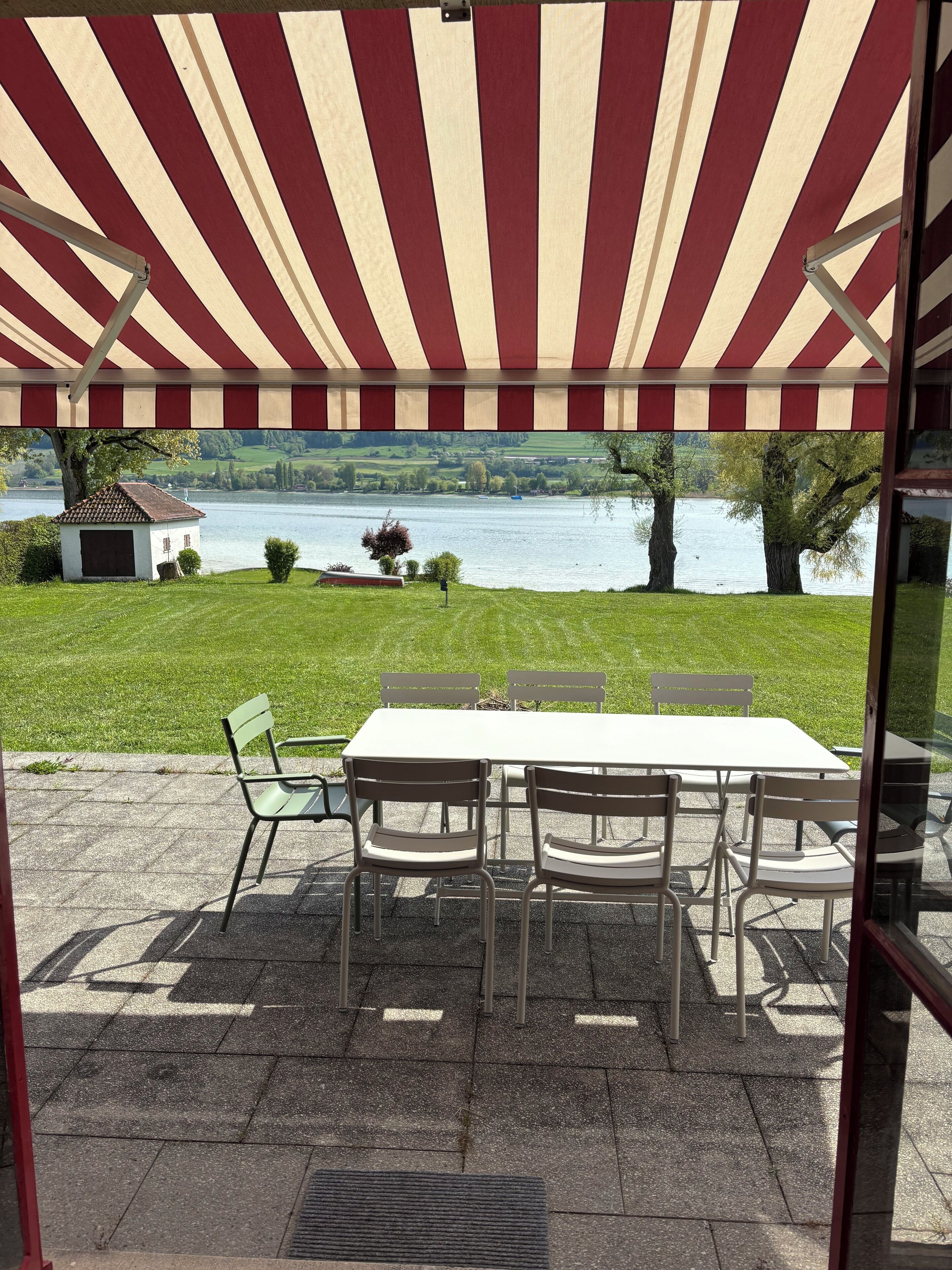 Une terrasse extérieure avec une table et des chaises, un auvent à rayures rouges et blanches, et une vue sur un lac.
