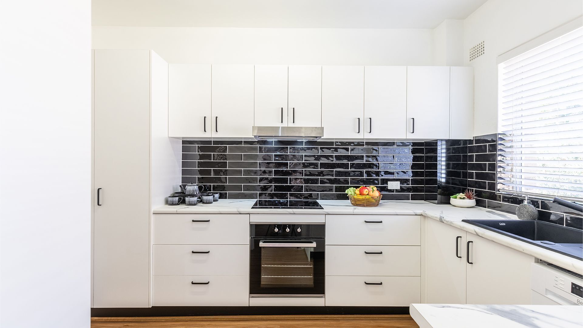 A modern kitchen with white cabinets, a black tiled backsplash, and stainless steel appliances.