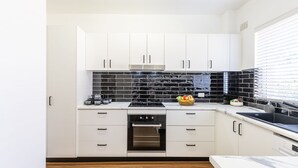 A modern kitchen with white cabinets, a black tiled backsplash, and stainless steel appliances. - Veronica Court 1, 4 Weatherly Cl - Aircon (Nelson Bay)