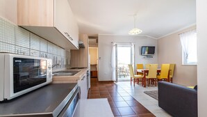 Eine moderne Küche mit Mikrowelle, Herd und Spüle. Ein Essbereich mit gelben Stühlen und einem an der Wand befestigten Fernseher.