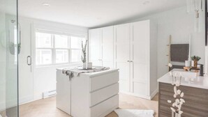 A modern bathroom with a glass shower enclosure, a white vanity with a dark countertop, and a large window providing natural light. - The QV Stage, Lux Couples Retreat W/ Outdoor Sauna (St. John's)