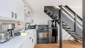Eine kleine Küche mit Toaster, Kaffeemaschine, Mikrowelle und Backofen. Ein Holzboden und eine schwarze Treppe sind ebenfalls zu sehen.