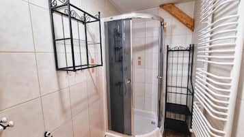 Baño con ducha esquinera, mampara de vidrio, estante metálico negro y toallero blanco.