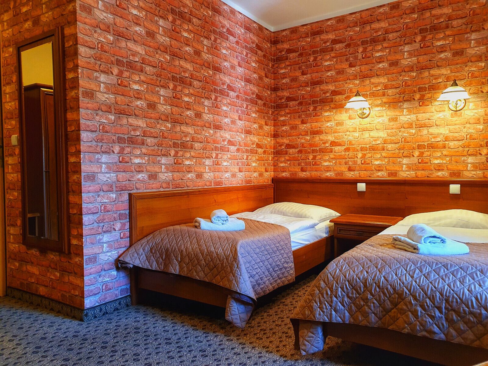 Habitació d'hotel amb dos llits, una paret de maó i dues làmpades penjades a la paret.
