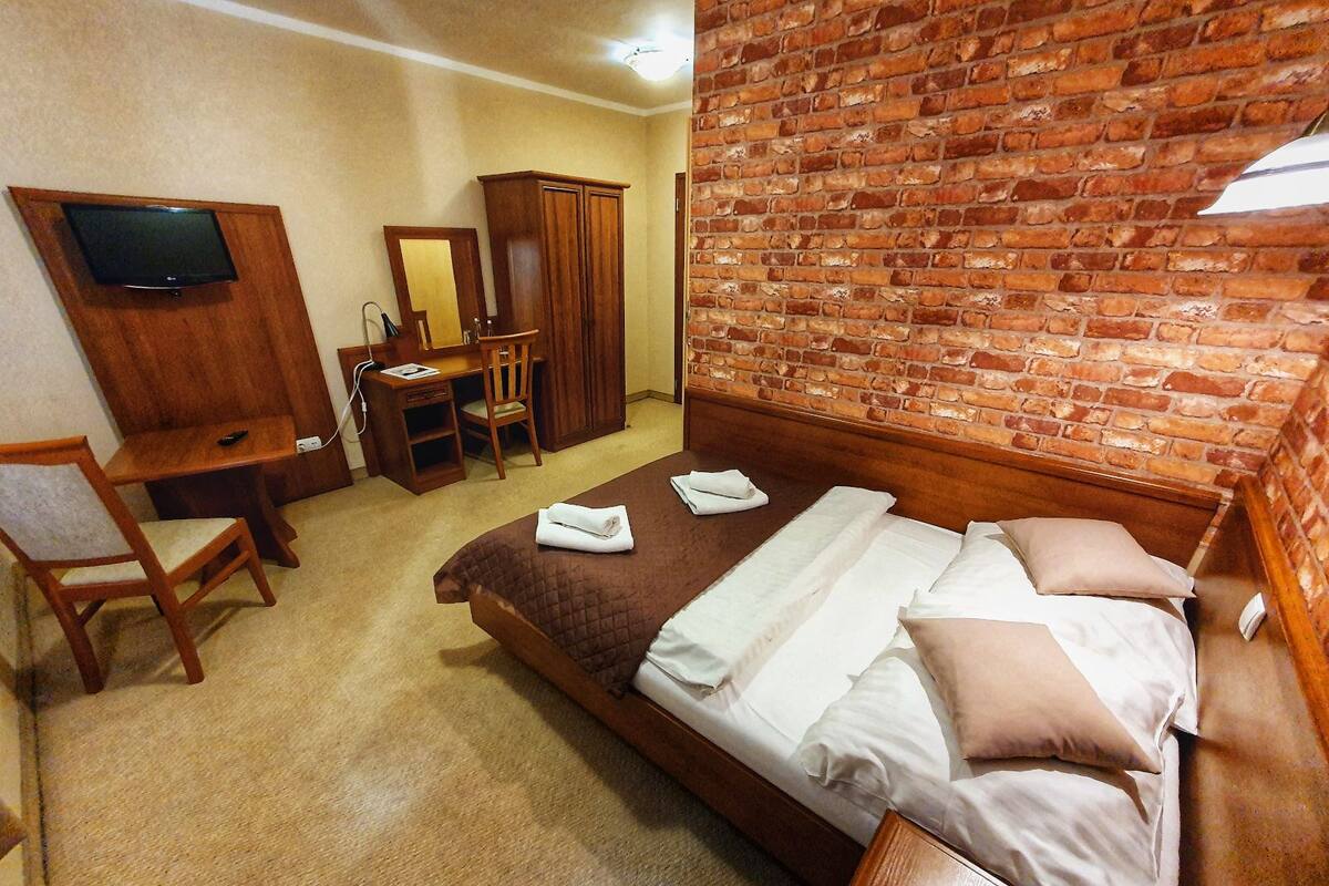 Une chambre d’hôtel avec un mur en briques, un lit avec des oreillers, un bureau avec une chaise, une armoire et un téléviseur fixé au mur.