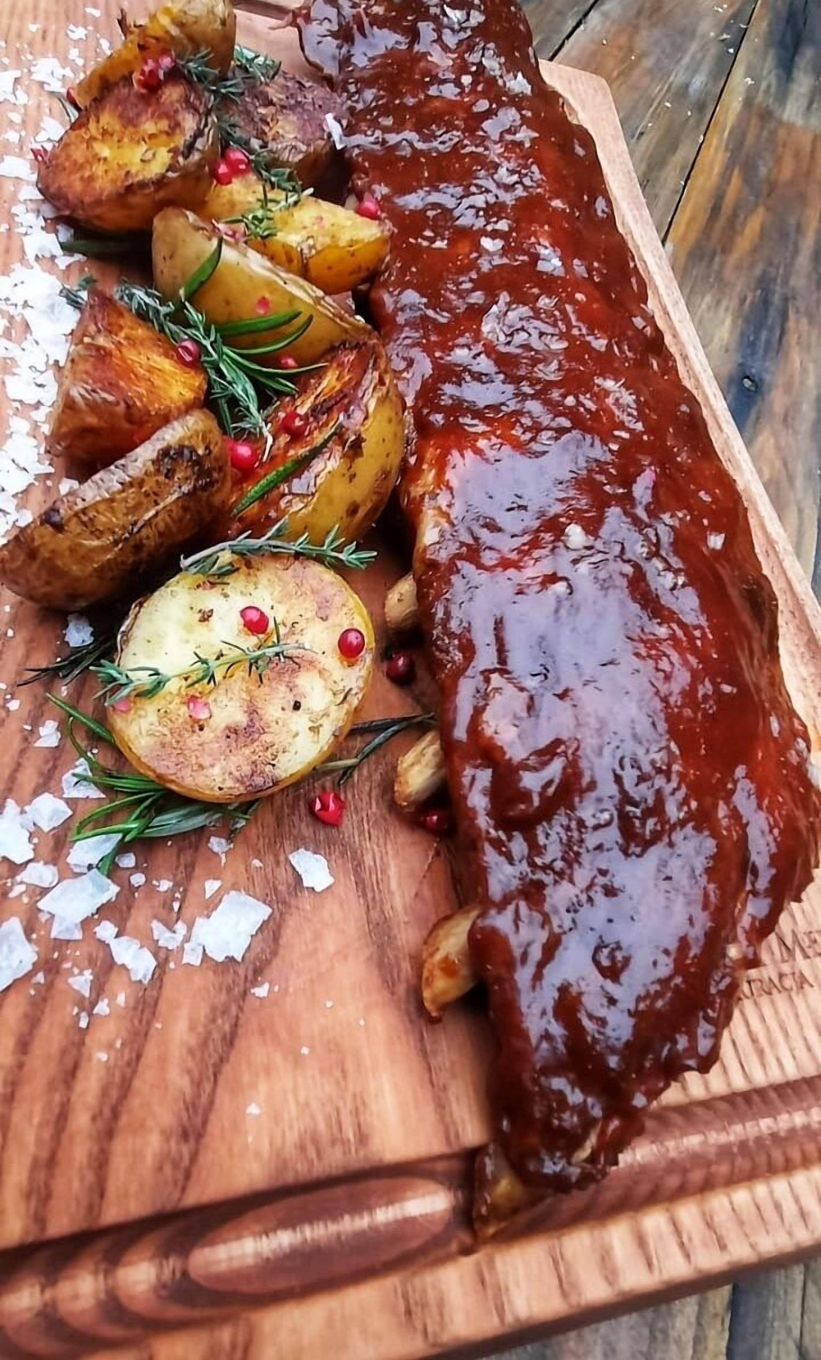 Una tabla de madera con un guiso de carne glaseada, patatas asadas y ramitas de romero.