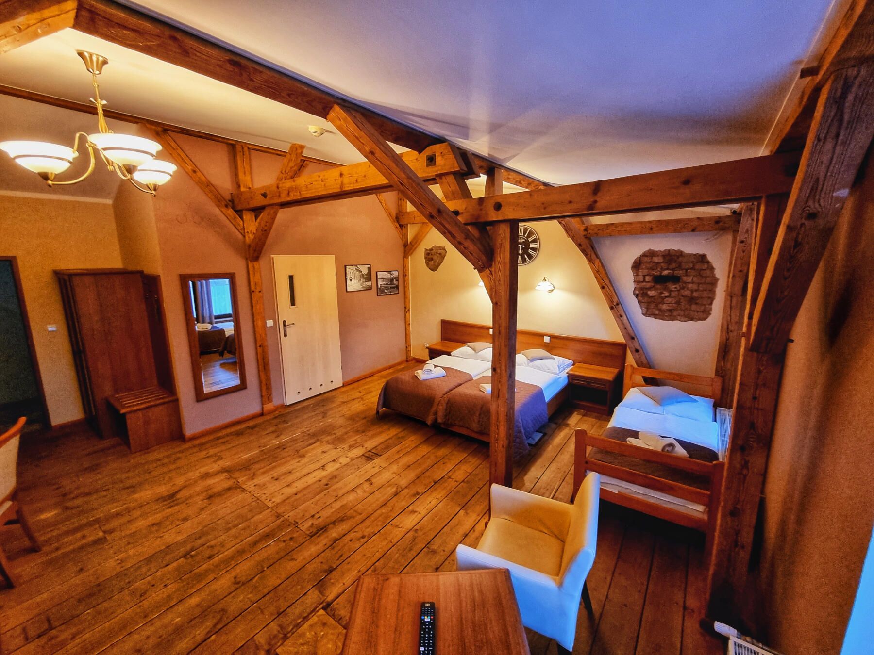 Una habitación rústica con vigas de madera, una araña, una cama con dos almohadas, una silla y una mesa de madera.