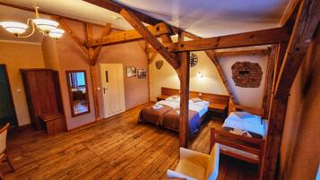 Una habitación rústica con vigas de madera, una araña, una cama con dos almohadas, una silla y una mesa de madera.