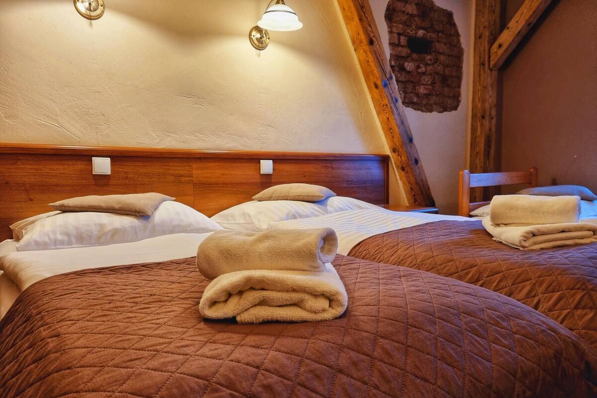 Une chambre d’hôtel avec deux lits, chacun recouvert d’une courtepointe marron matelassée et agrémenté de serviettes soigneusement pliées.