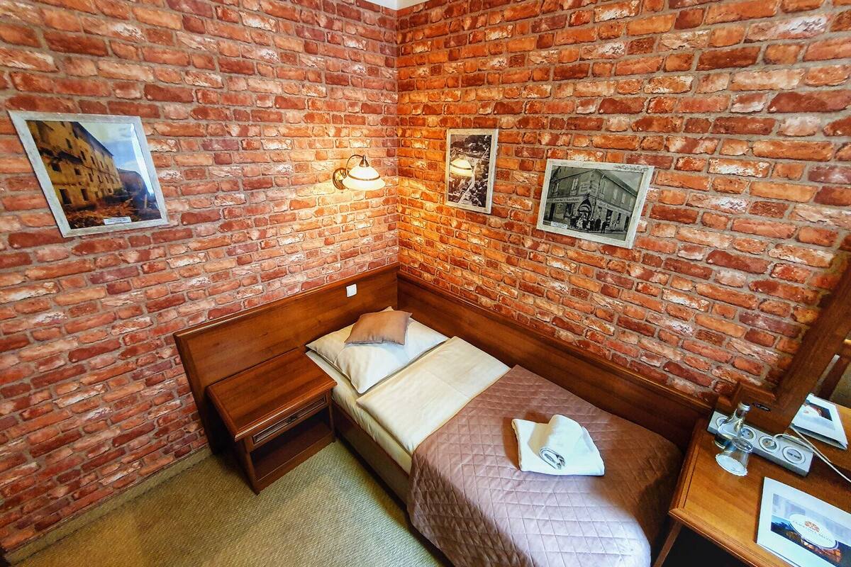 Une petite pièce accueillante avec un mur en briques, un lit en bois, une table de chevet et une petite table avec une lampe.