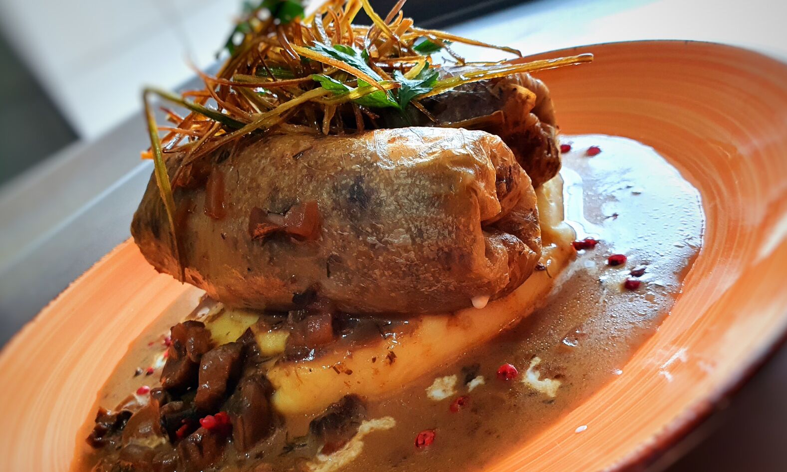 A dish with a roasted meat centerpiece, garnished with herbs, served on a plate with a sauce and vegetables.