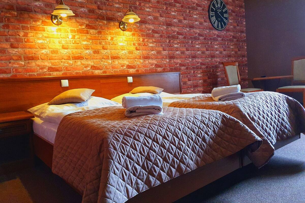 Une chambre d’hôtel avec deux lits, un mur en briques et une horloge.