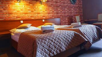 A hotel room with two beds, a brick wall, and a clock.