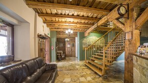 Un vestíbulo con techo de madera, una escalera, un sofá de cuero y suelo de piedra.