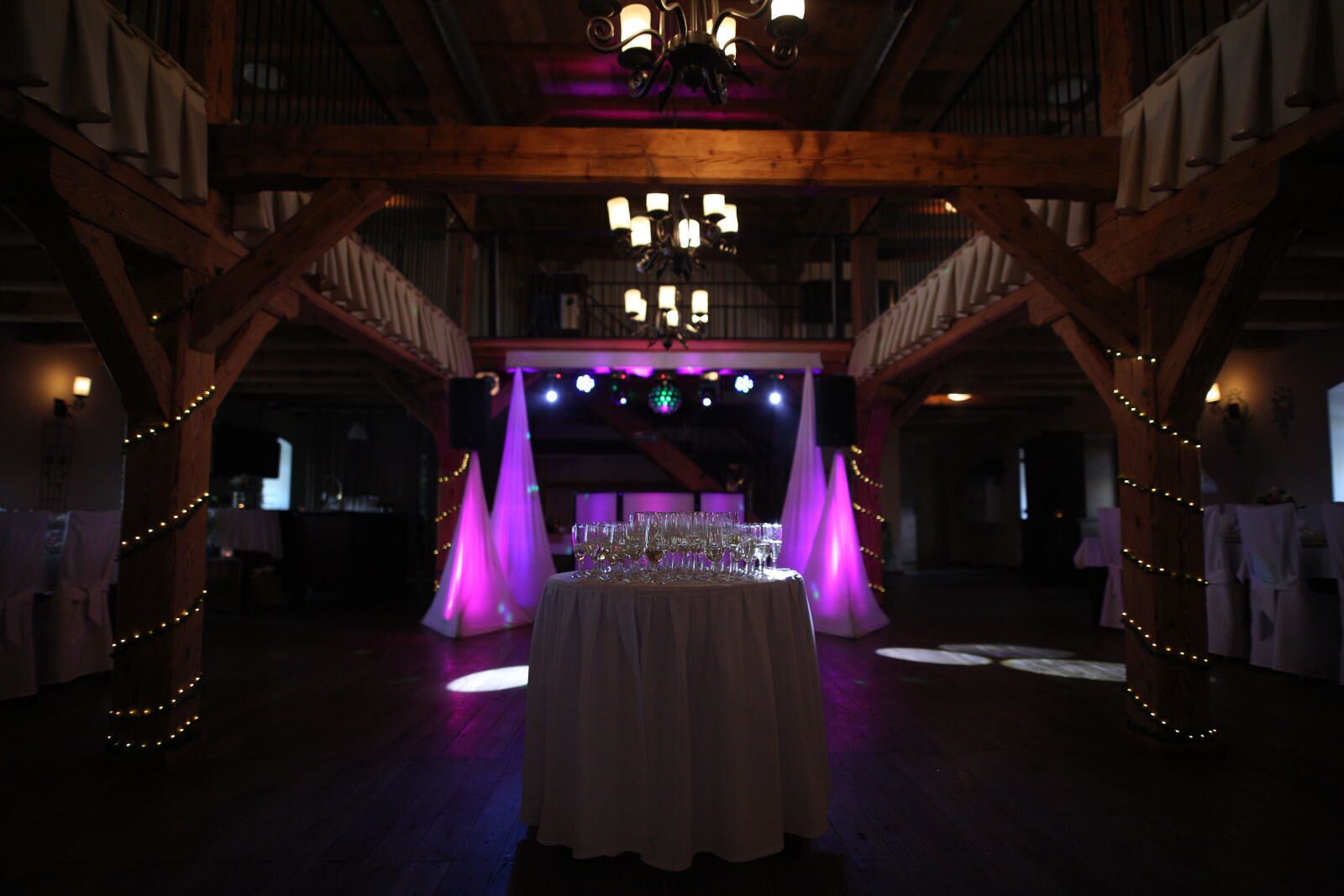 A banquet hall with a long table set for a formal event, wooden beams, and a chandelier.