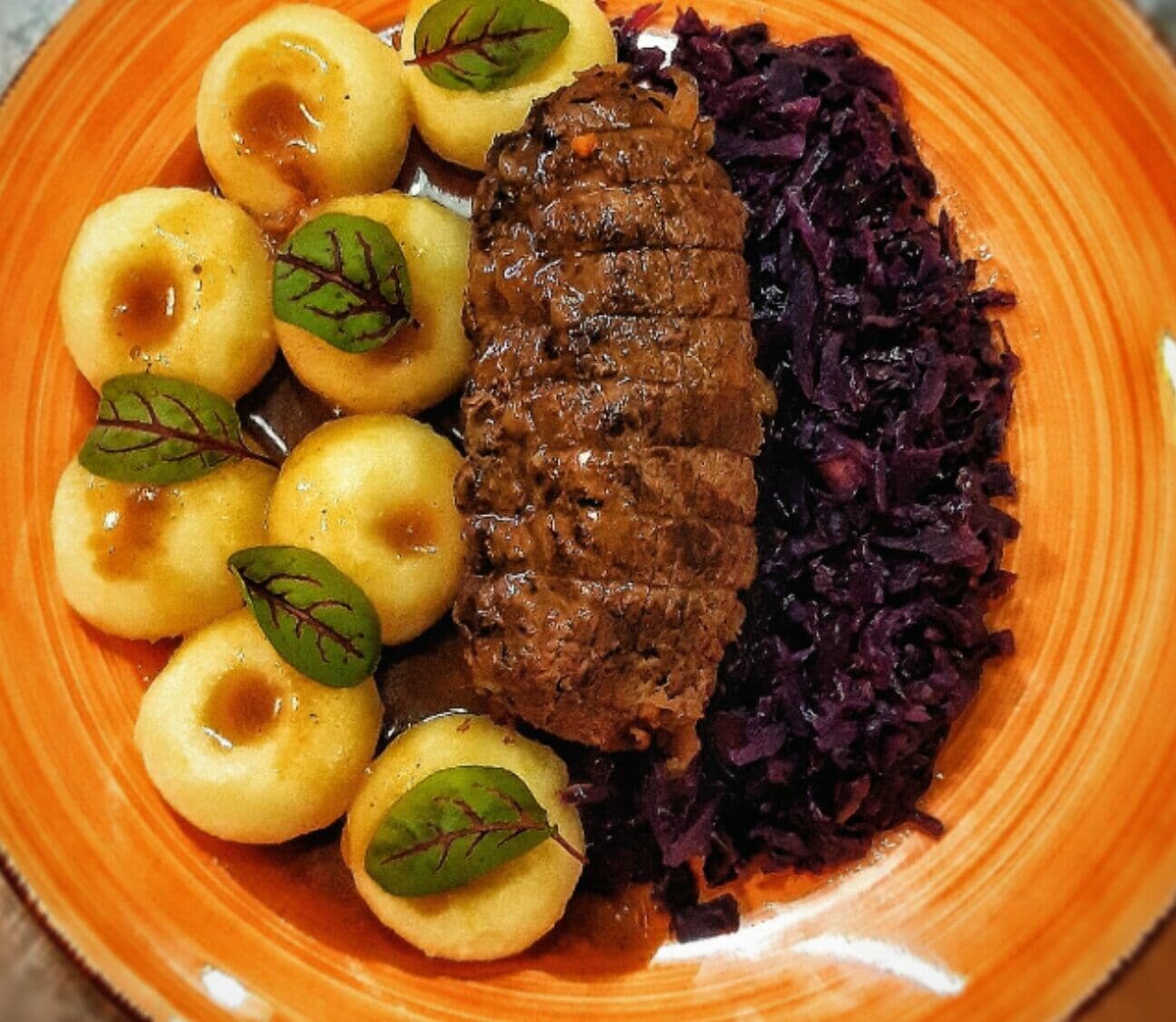 En tallerken med bøf, kogte kartofler og rød kål.