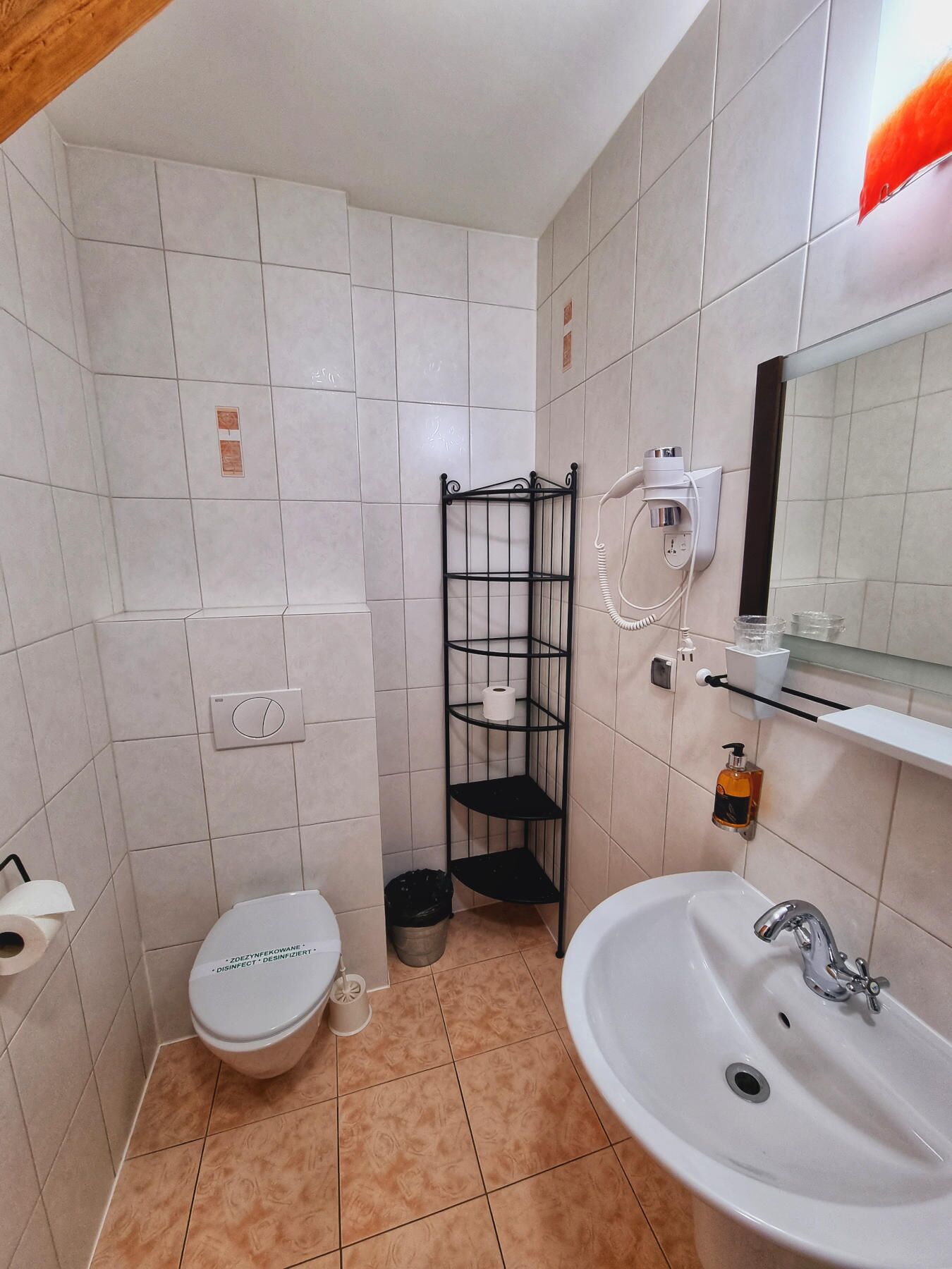 Un baño pequeño con inodoro, lavamanos y un estante metálico.