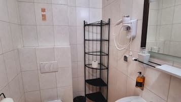Un baño pequeño con inodoro, lavamanos y un estante metálico.