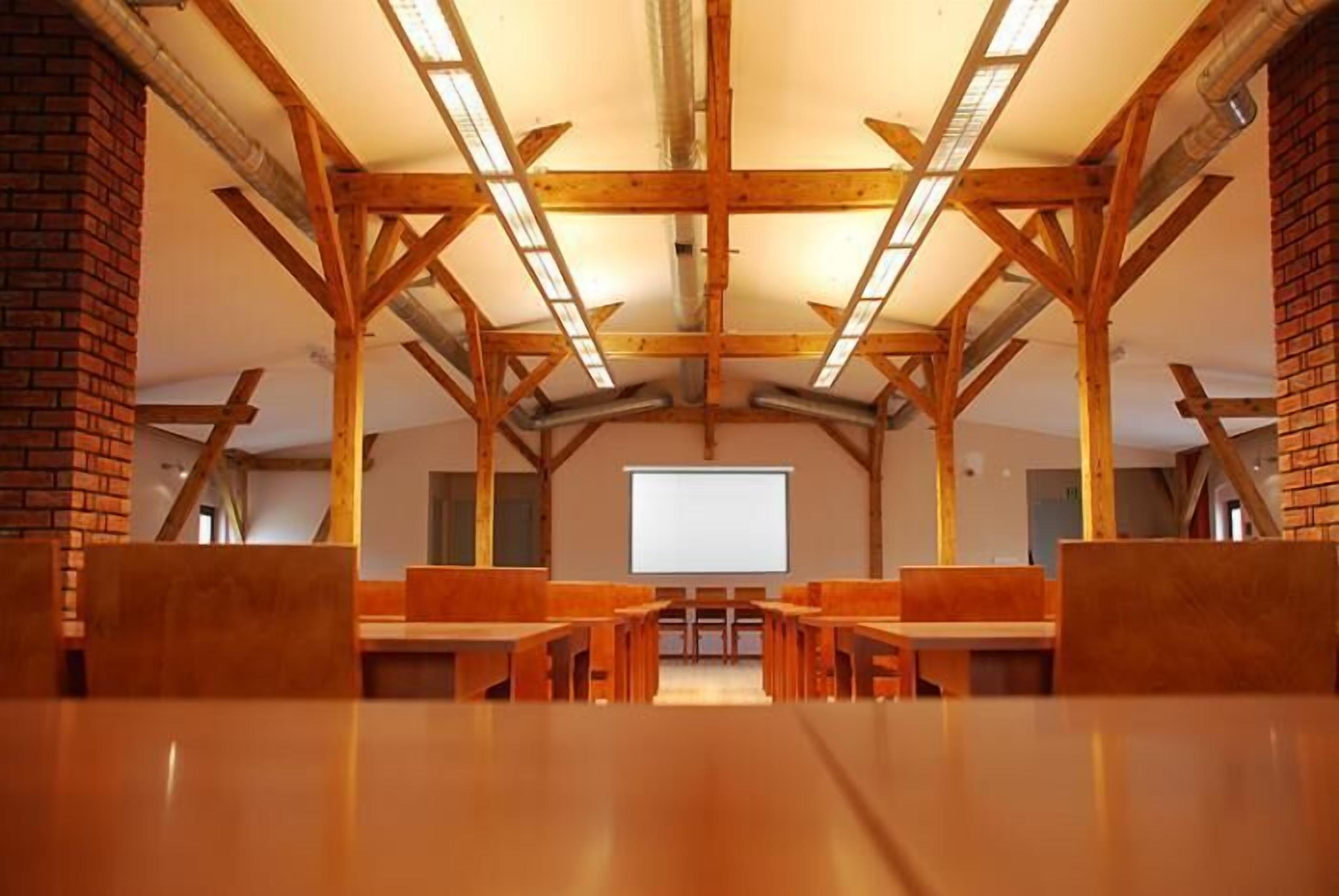 A conference room with wooden beams, a projector screen, and multiple tables and chairs.