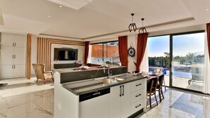 Une cuisine moderne dotée d’un îlot central, d’un coin repas avec une table et des chaises, d’une grande fenêtre offrant une vue dégagée et d’un plafond pourvu d’un éclairage encastré.