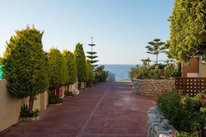 A pathway leading to a beach with neatly trimmed trees and a stone wall on one side.