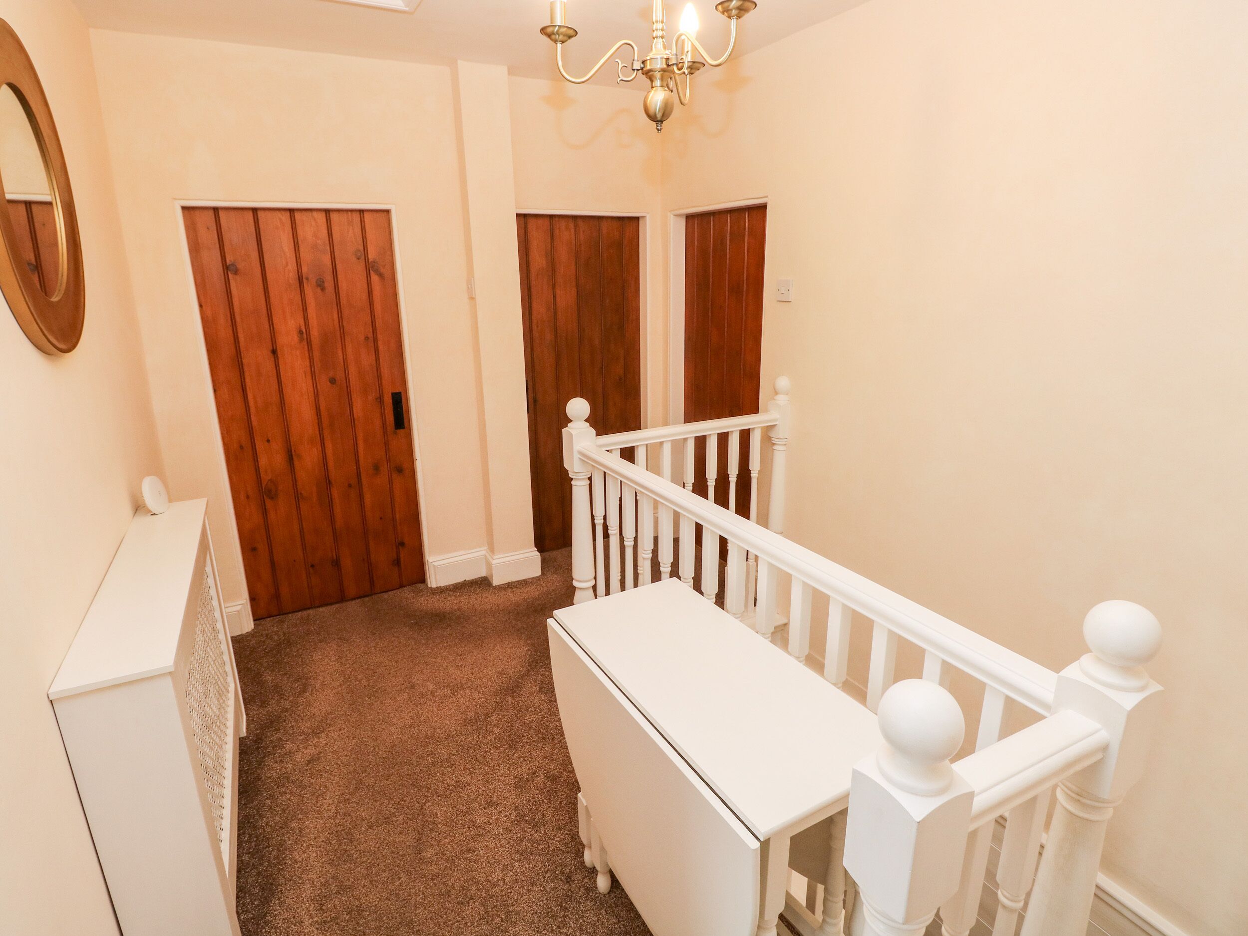 A hallway with a carpeted floor, wooden doors, a white dresser, and a white railing.