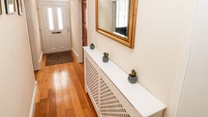 Um corredor com um espelho grande, um console branco e uma porta no final.