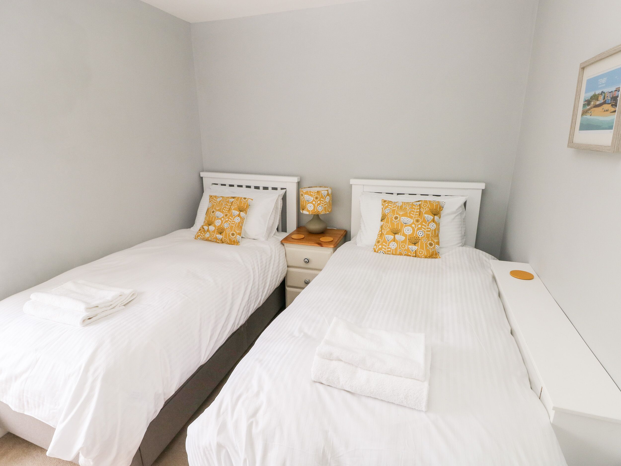 Two single beds with white bedding and yellow patterned pillows in a room with light-colored walls.