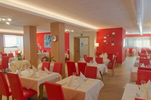 Un restaurante con sillas rojas y mesas blancas, un reloj en la pared y una puerta al fondo.