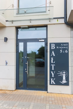 Une entrée d’immeuble avec une porte en verre, une enseigne indiquant « BALTYK » et une petite fenêtre au-dessus de la porte.