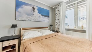 Un dormitorio con cama, mesita de noche, lámpara, ventana con cortinas y un cuadro colgado en la pared de un faro.
