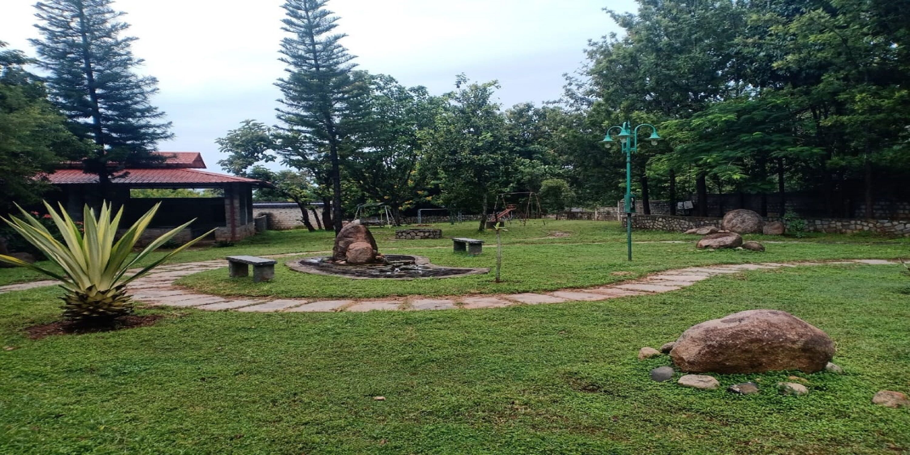 A well-maintained garden with a circular stone path, a central water feature, and a variety of trees and shrubs.