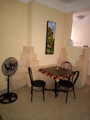Enjoy meals in this cozy dining area with a table and two chairs, a standing fan, and a shelf for your wine glasses.