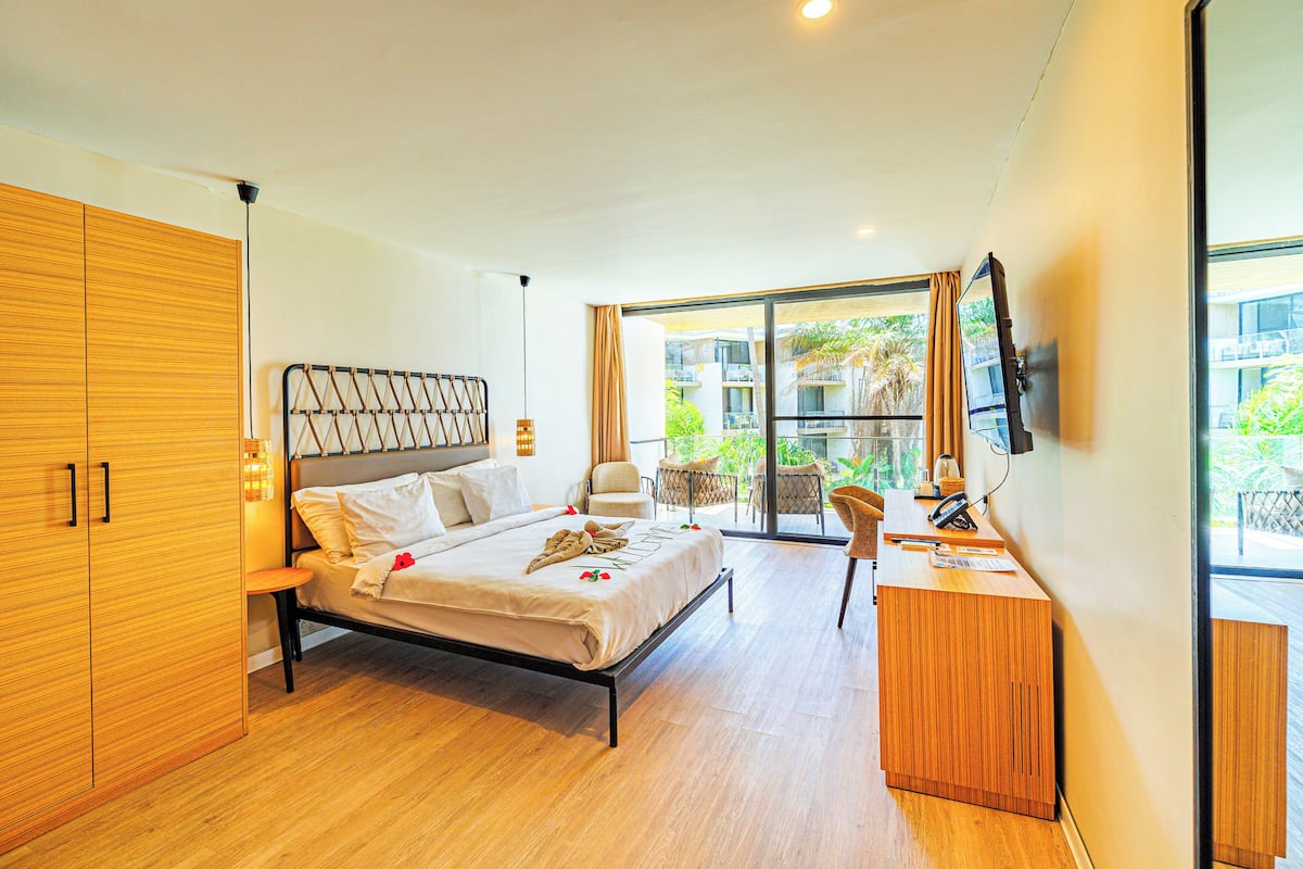 Un dormitorio moderno con cama, armario de madera, escritorio y un balcón con mobiliario exterior.