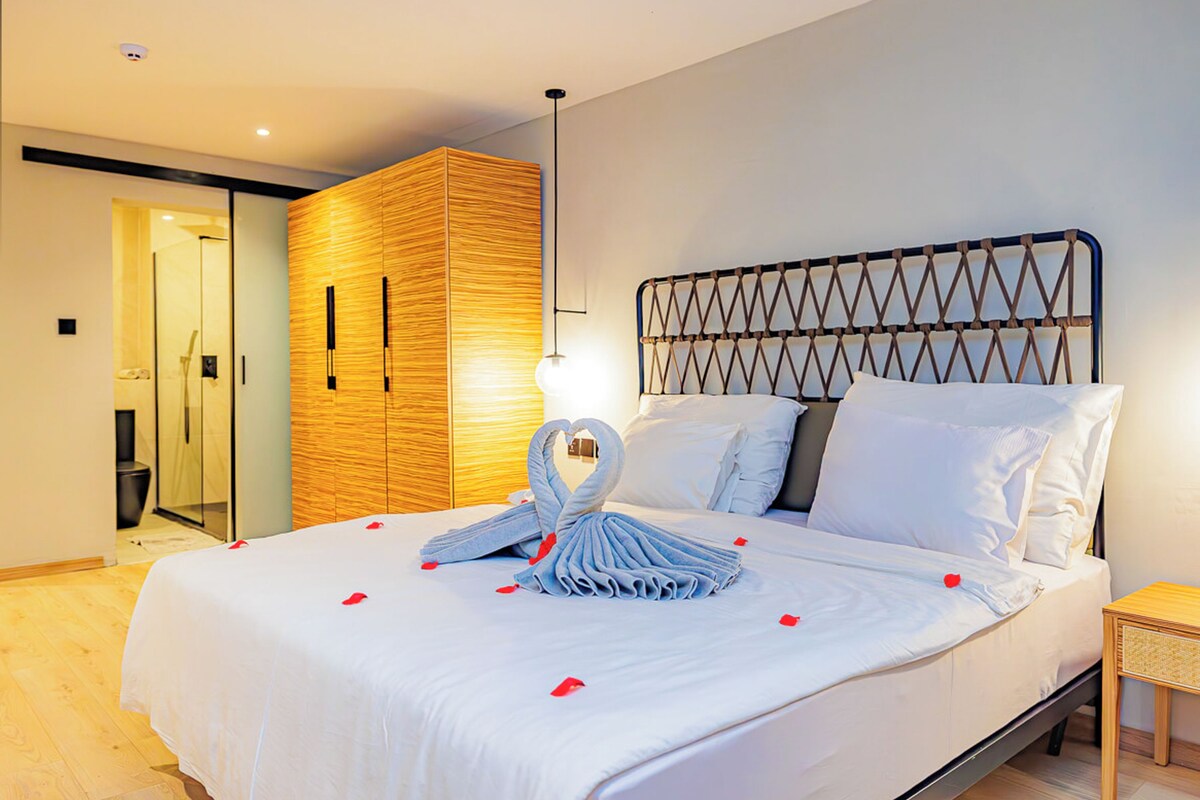 A modern hotel room with a large bed, a wooden wardrobe, and a glass shower enclosure.