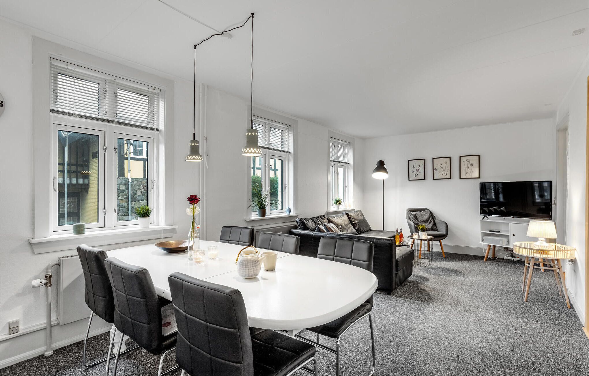 A modern living room with a white dining table, black leather sofa, and a TV.