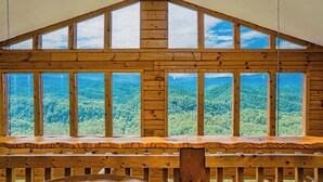 A wooden cabin with large windows offering a view of a forested mountain range. - PinnacleView: POOL, Breathtaking Views, Movie Room, Games, Hot Tub, Wifi (Sevierville)