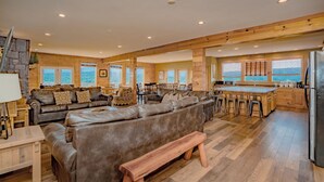 Uma sala de estar ampla, com um sofá grande, um banco de madeira e uma cozinha com armários de madeira e uma ilha central.