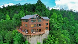 A multi-story wooden cabin with a balcony, surrounded by dense forest. - CrestView: POOL, MtnViews, Secluded, Theater, Games, Hot Tub, Wifi, Large Groups (Sevierville)