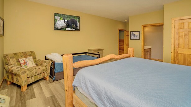 A bedroom with a wooden bed, a wooden chair, a small bedside table, and a wall-mounted picture. - CrestView: POOL, MtnViews, Secluded, Theater, Games, Hot Tub, Wifi, Large Groups (Sevierville)
