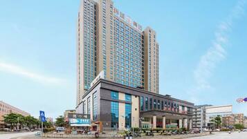 A high-rise hotel with a modern facade, a central entrance, and a parking area in front.