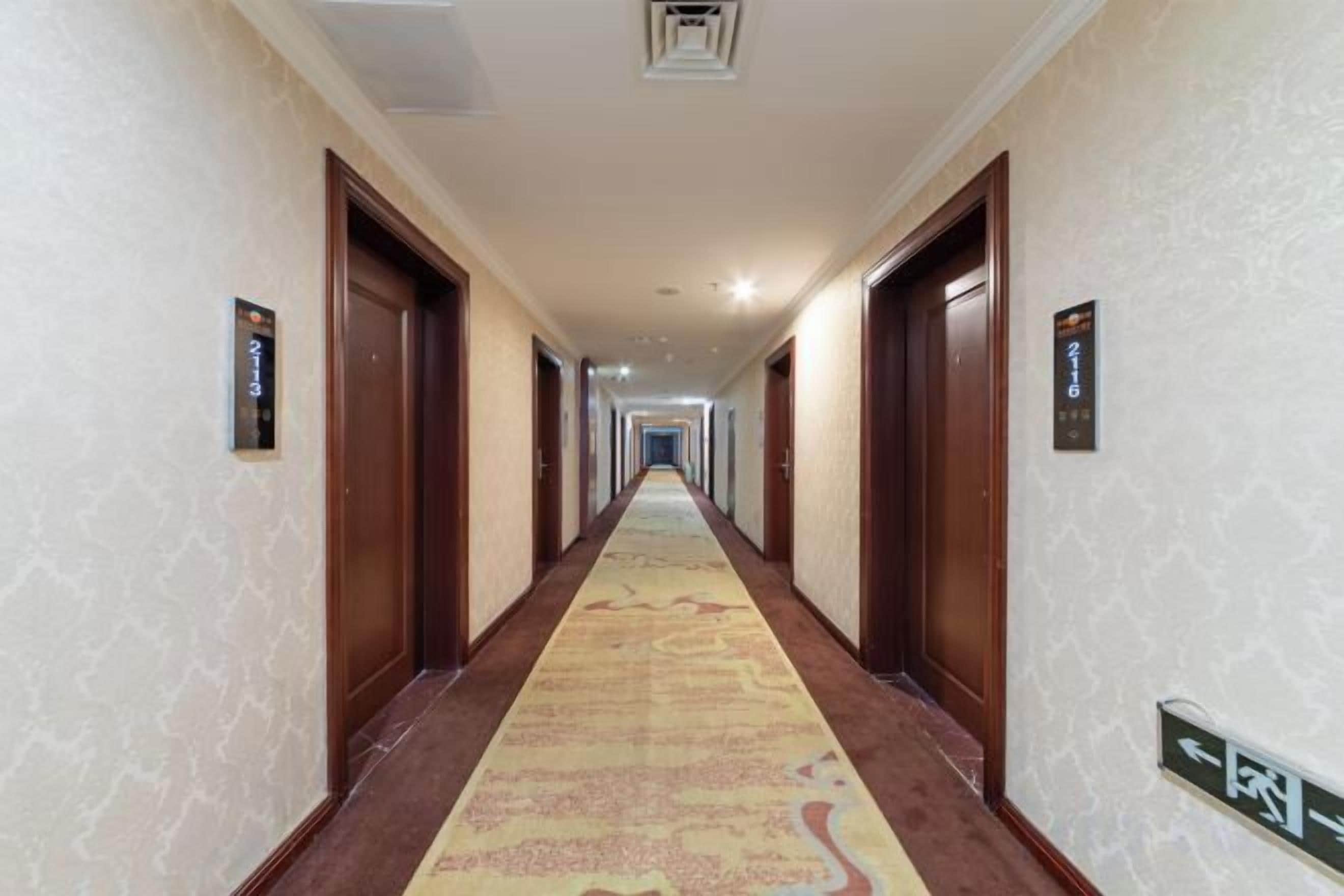 A hotel hallway with carpeted floors, wooden doors, and directional signs on the walls.