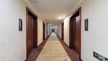 A hotel hallway with carpeted floors, wooden doors, and directional signs on the walls.