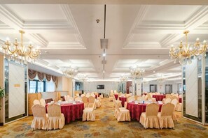 Una sala da banchetto con tavoli rotondi, sedie, lampadari e pavimento tappezzato.