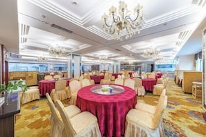 Un salón de banquetes con mesas redondas, sillas y candelabros.