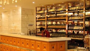 A wine bar with shelves of wine bottles, a counter with a person behind it, and a marble wall in the background. - Jingxi Global Hotel (Jingxi)