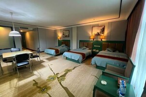 Habitación de hotel con dos camas individuales, un escritorio con sillas, una mesita pequeña y una botella de agua en la mesita de noche.